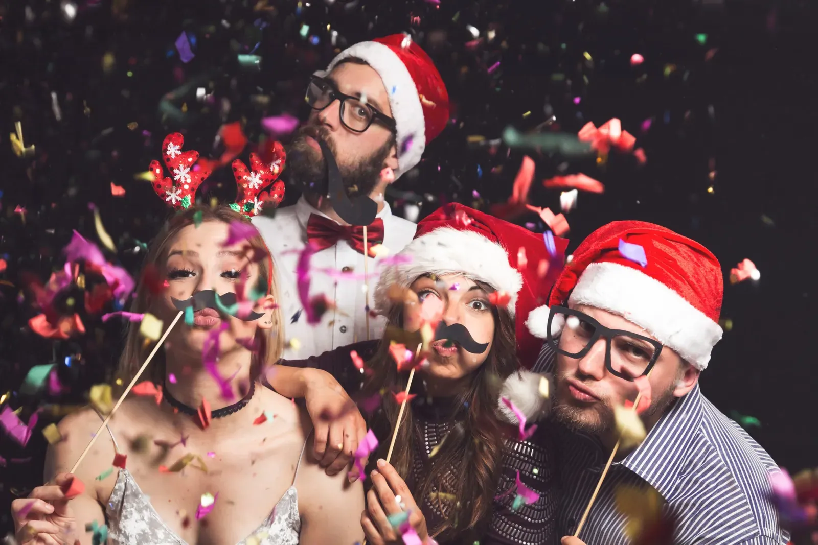 Four young friends having fun at New Year’s Eve Party, posing for photos with masks