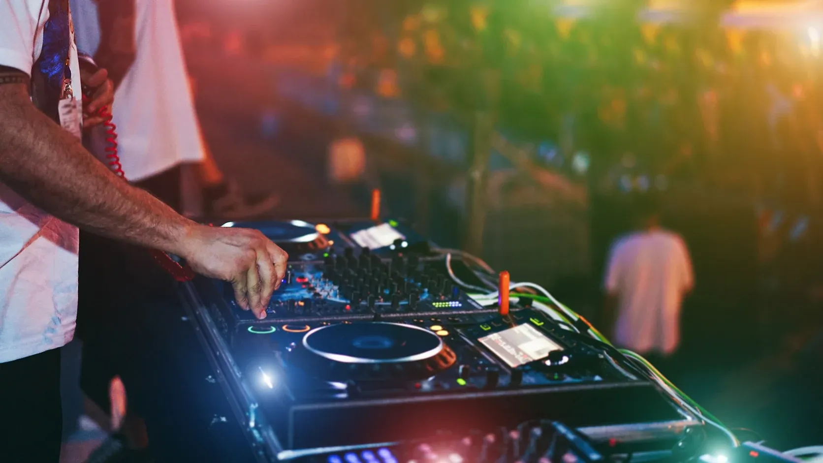 A DJ working the decks under coloured lighting in a busy late-night venue