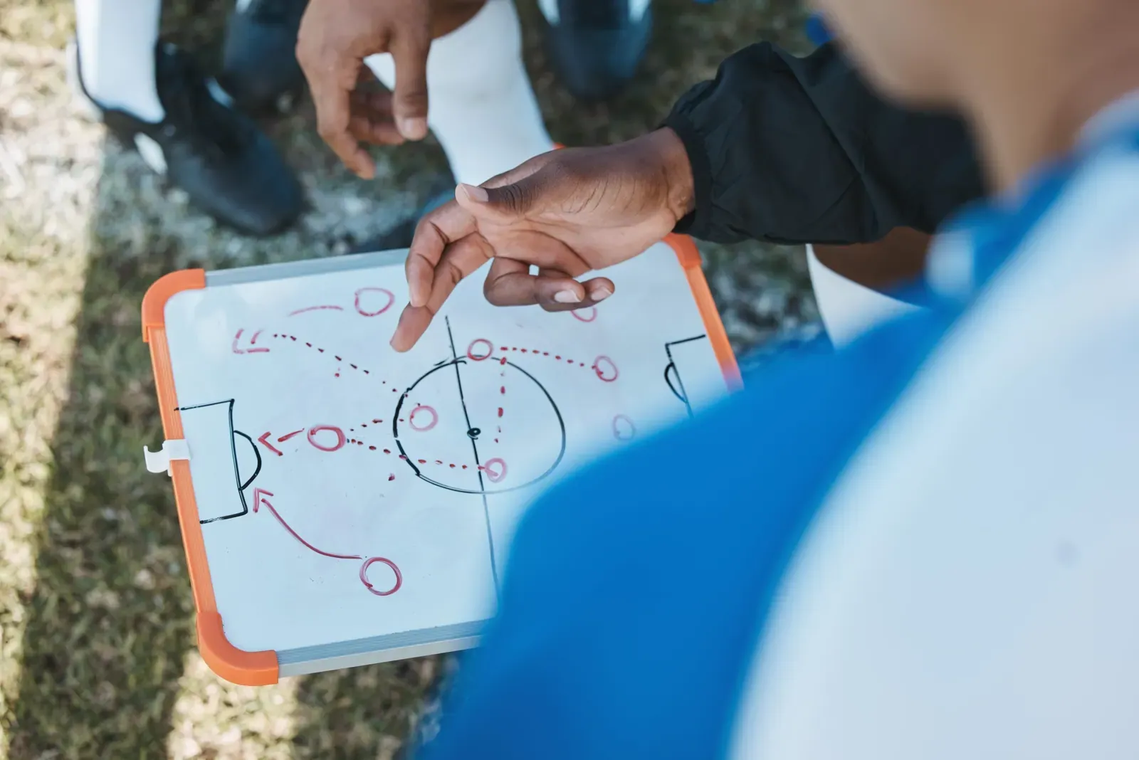 Hands, soccer team or coach planning a strategy with tactics or training formation on sports field. Board, fitness or closeup of manager teaching football players a game plan for match or workout.