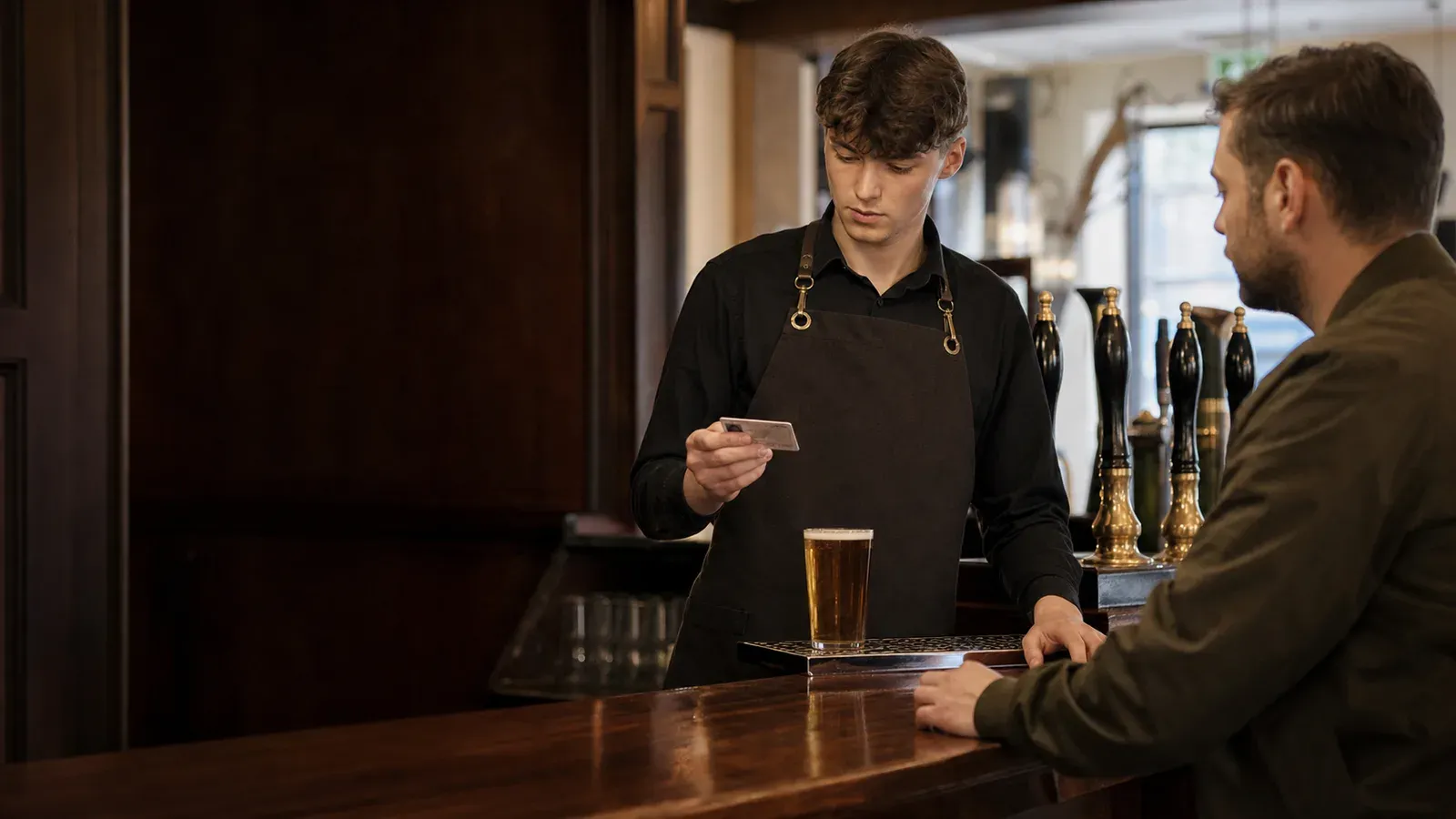 A bartender pouring a pint of beer behind a pub bar