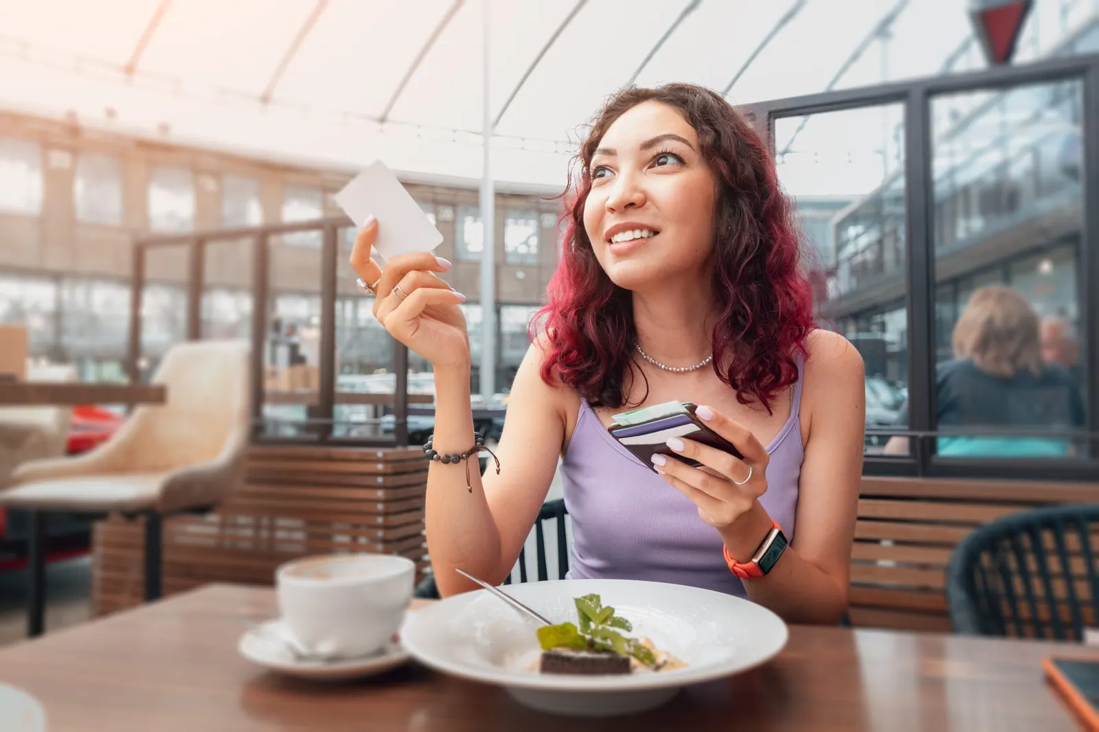 Happy girl raised her hand and calls the waiter to pay for breakfast in the cafe with a credit card