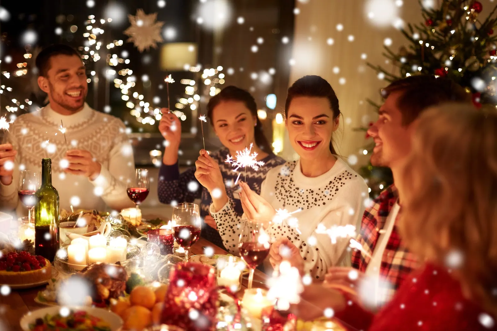 winter holidays and people concept – happy friends with sparklers celebrating christmas at home feast over snow